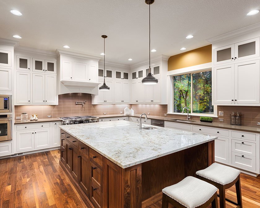Modern kitchen with white cabinets, beige backsplash, wooden floor, large wooden island with white marble countertop, and modern lighting above.