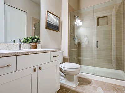 Small, modern bathroom with white cabinets, large mirror, tiled floor, and shower with glass door.