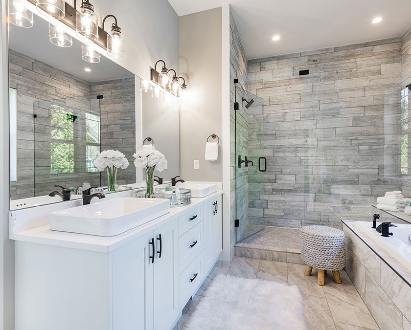 Upscale bathroom with white cabinets, large mirrors, quartz countertop, gray carpet, and large shower with glass walls.