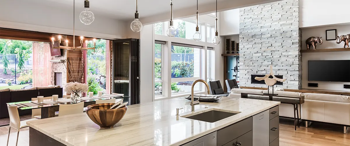 A kitchen island with a beautiful white counter and overhead lights