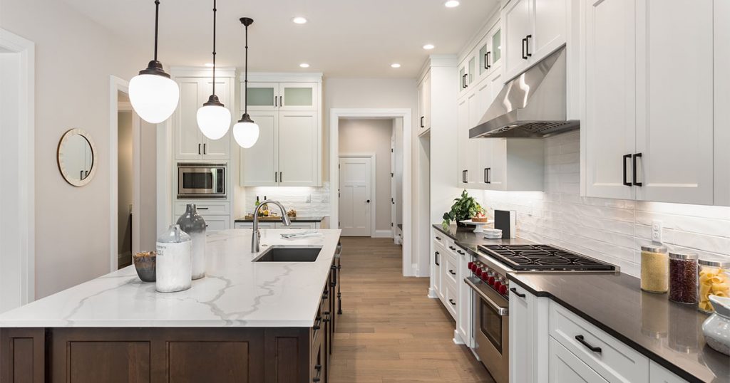 A marble countertop with overhead lighting and white kitchen cabinets
